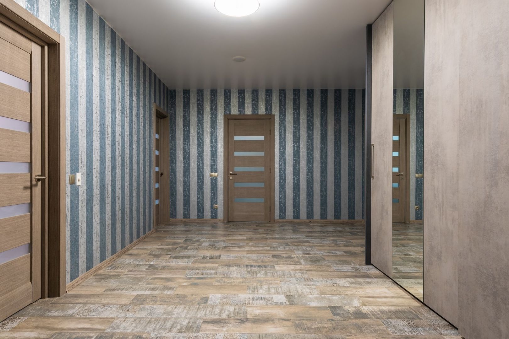 Hall med träliknande klinkergolv, randiga väggar och flera trädörrar