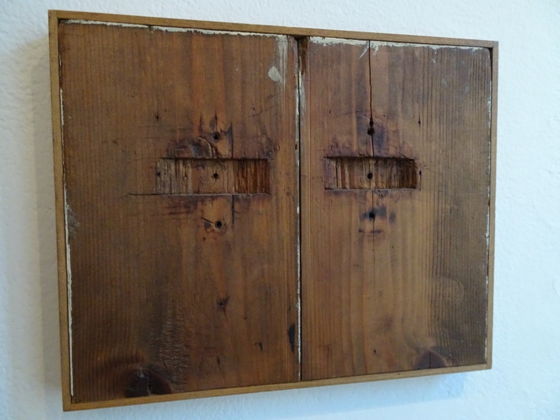 En väggmonterad träpanel med två sektioner av åldrat trä som visar naturliga skavanker, sprickor och slitagemönster. Träet har en varm brun ton och visas mot en vit vägg, vilket exemplifierar wabi-sabi-estetiken att finna skönhet i det ofullkomliga.