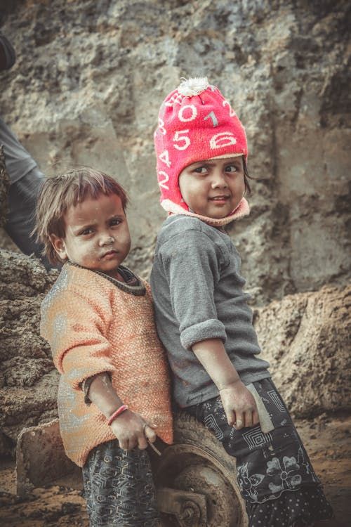 Två barn i varma kläder utomhus, en med röd mössa.